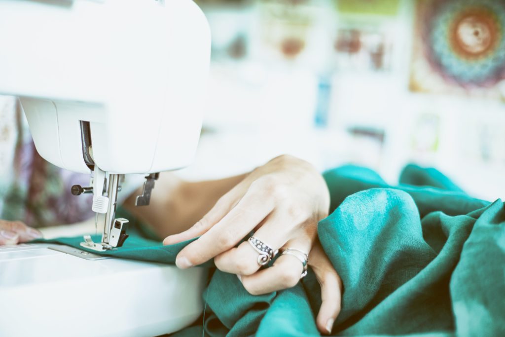 main de couturière tenant un tissu vert sur une machine à coudre